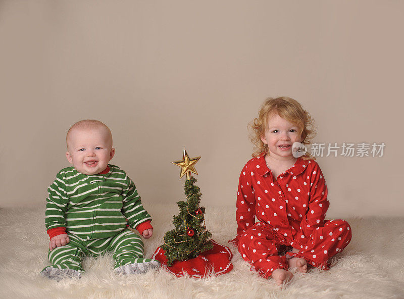 穿着睡衣的男孩和女孩坐在圣诞树旁