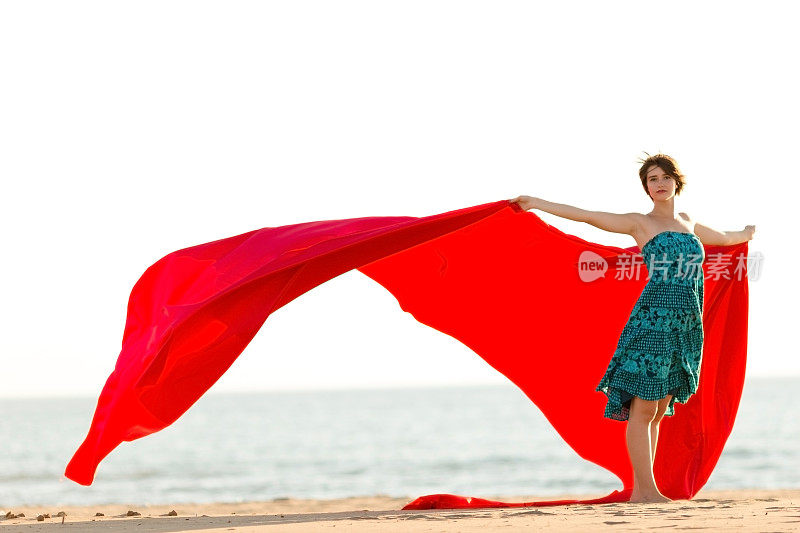海滩上穿着飘动的红色织物的女人