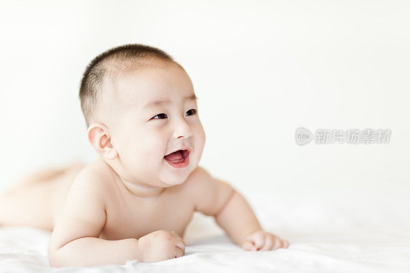 赤裸快乐的小男婴爬在白色的床上