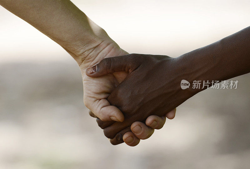 白人妇女和非洲女孩手拉手是友谊的象征