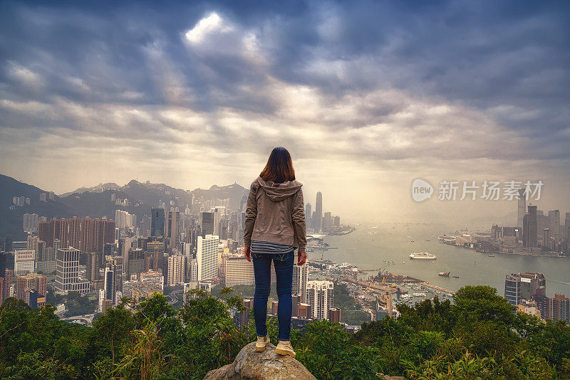 女孩与背包客享受阳光在山顶雾蒙蒙的城市。山顶上的岩石和日落在香港城市。成功,冠军,领袖的概念。