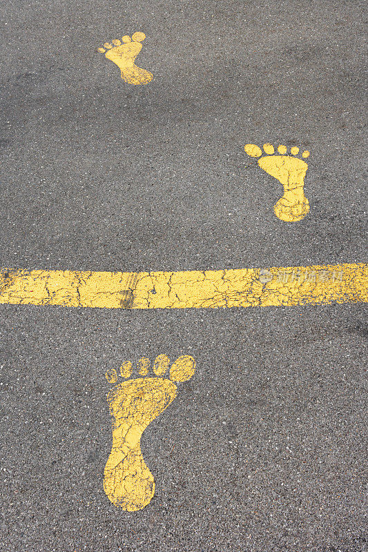 柏油路上有三个黄色脚印，越过一条线