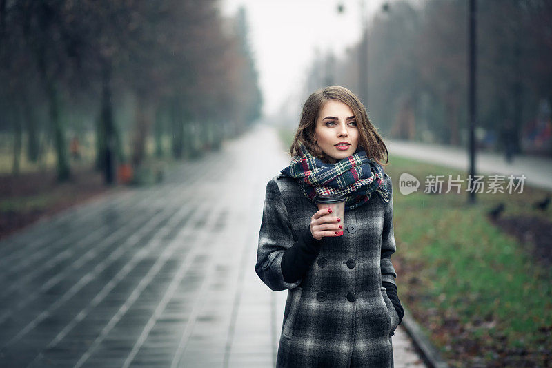 年轻的成年女性与一杯咖啡在城市公园;