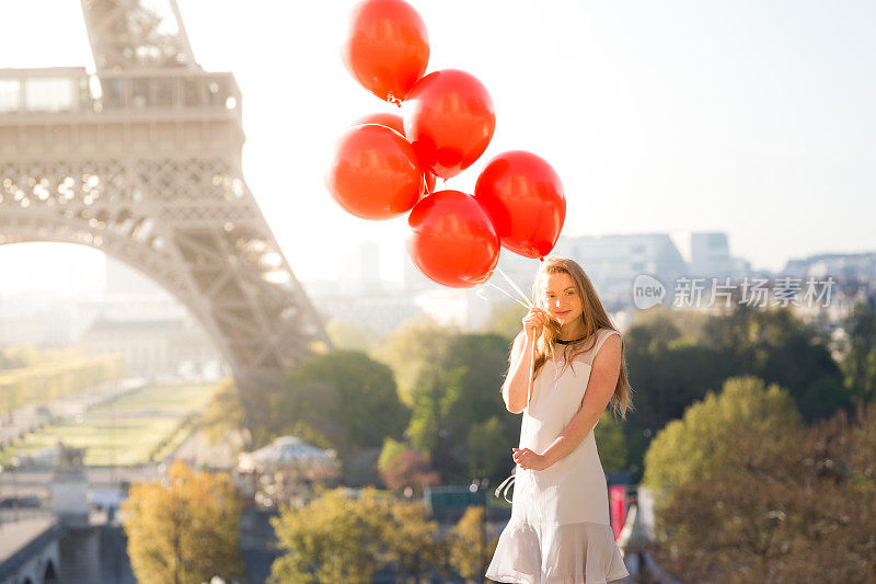 在埃菲尔铁塔附近，一个女孩拿着一堆红气球
