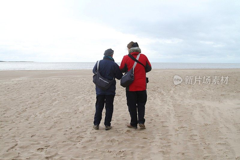 两个男人在寒冷的天气在海滩上的后视图