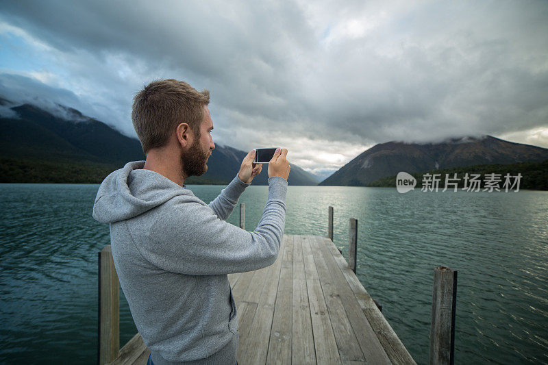 游客站在湖边码头，用手机拍照