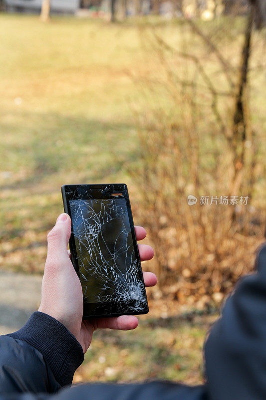 人类手握智能手机碎屏。户外手握碎裂手机。黑色手机坏在手里。破碎的手机和破碎的屏幕，近距离。