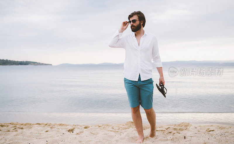 一个英俊的大胡子男人在一个美丽的夏日的海滩上