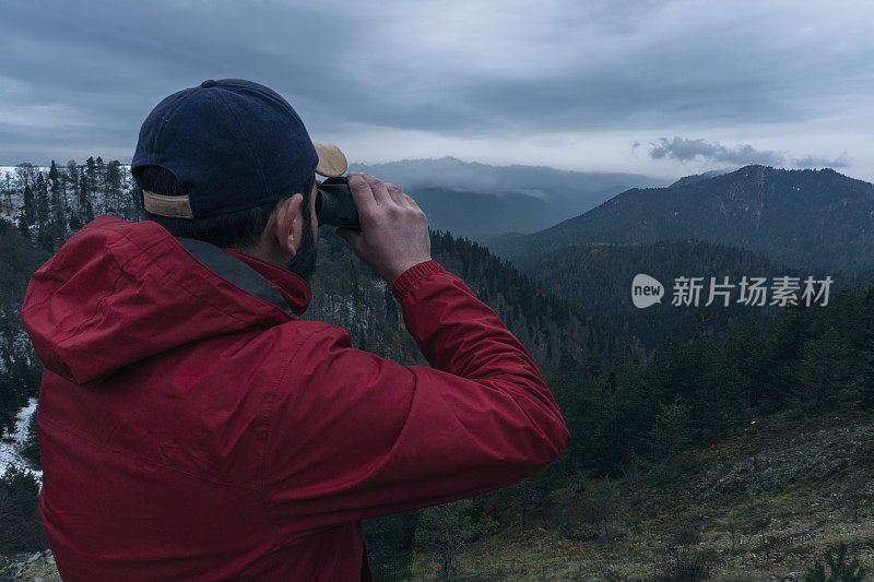 一个年轻人站在山顶上，用望远镜看