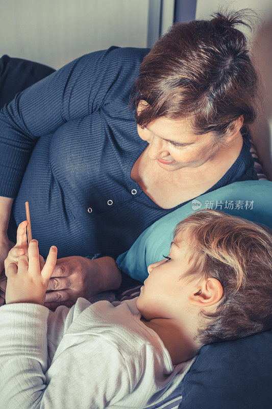 小男孩和他的祖母在睡觉前使用智能手机。