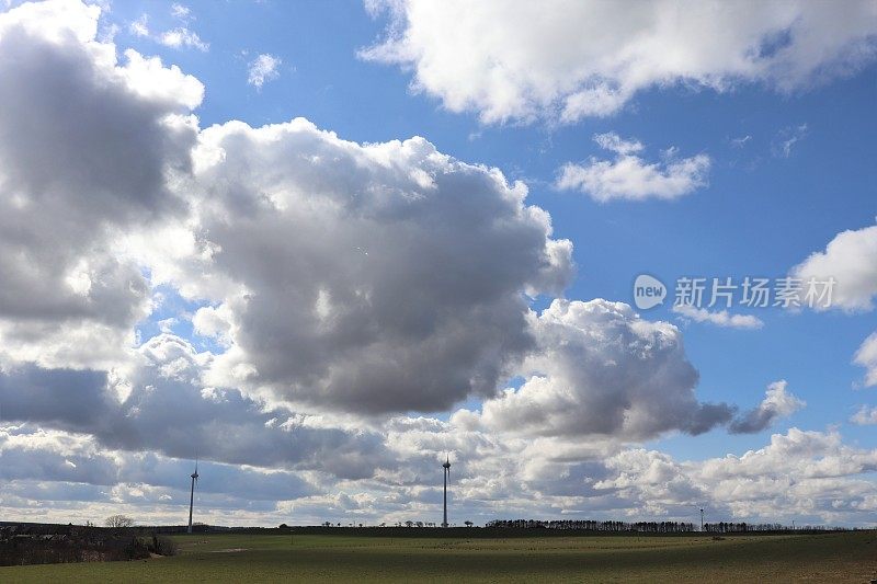 在乡村环境中，蓝天映衬着蓬松的白云，还有风力涡轮机或乡村公路