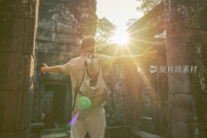 一名年轻男子在柬埔寨参观吴哥窟的庙宇，他张开双臂站着。人们旅游发现亚洲的概念。日落时分，只有一个人，在东南亚暹粒冒险和探险。