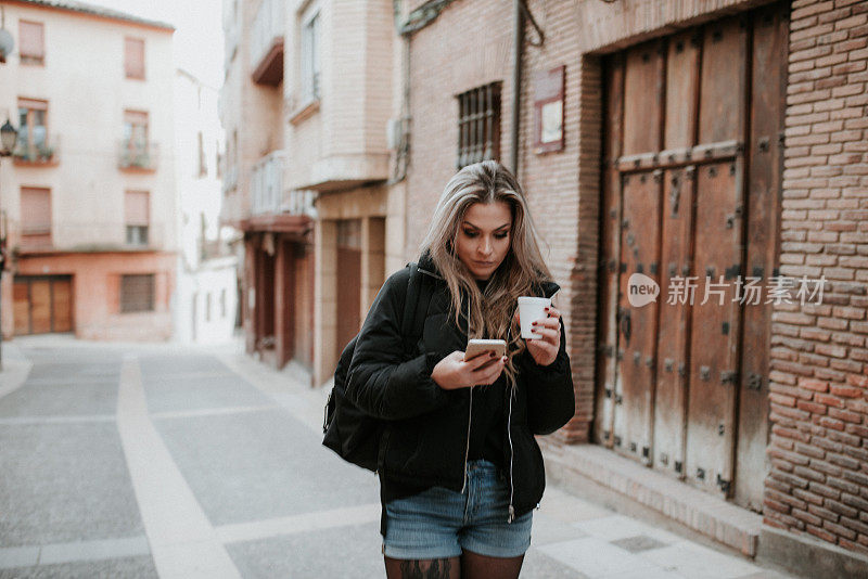 年轻女子拿着外带咖啡杯看着智能手机