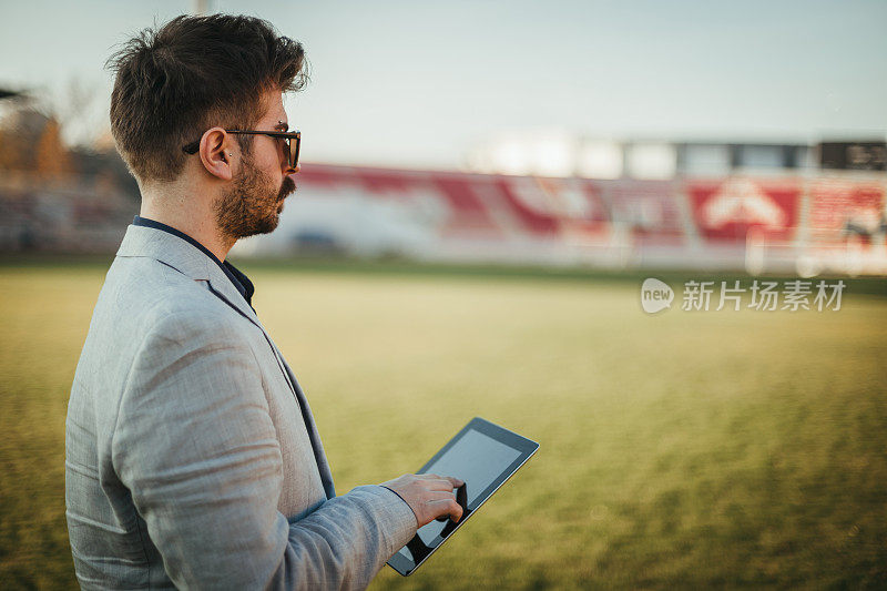 年轻的商人在足球场上使用数字平板电脑