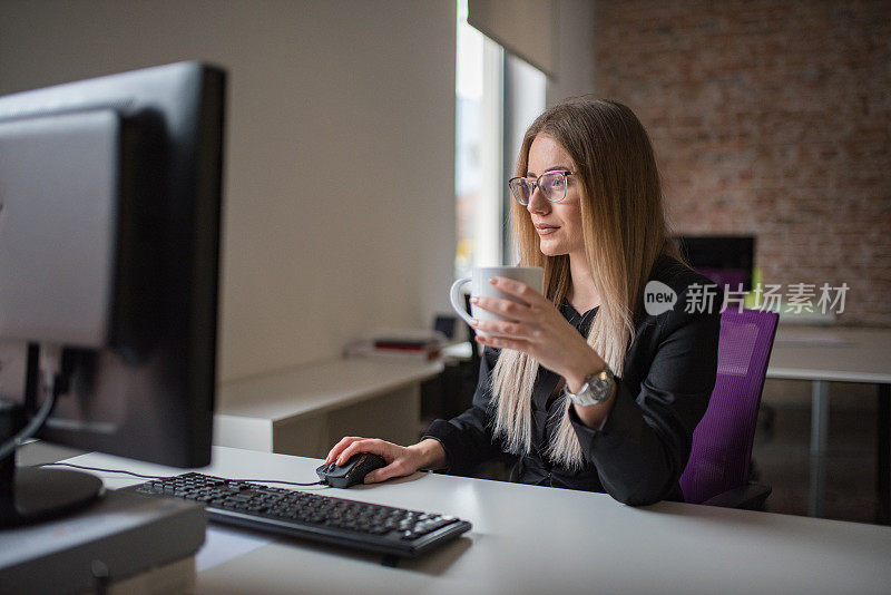 女商人用电脑，在办公桌前喝咖啡