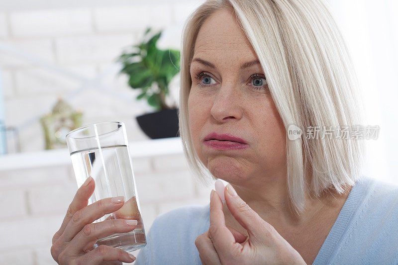 中年妇女握着玻璃杯、静水和药丸。患者口服止痛药或抗生素药丸，治疗慢性抑郁症或生物活性补充概念