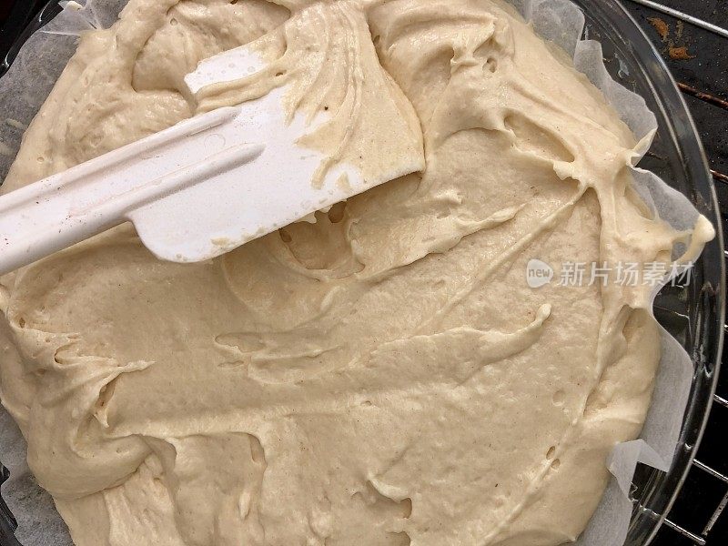 用塑料抹刀将香草维多利亚海绵蛋糕的面糊涂在不粘蛋糕罐里，内衬有防油纸
