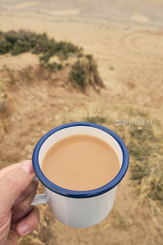 在康沃尔纽基的康沃尔海岸，手持一个盛满茶的锡杯。