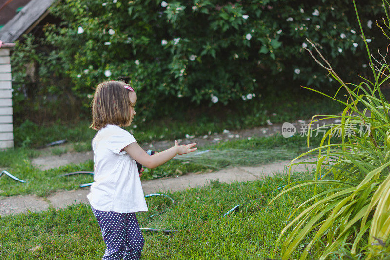 可爱的小女孩夏天在花园里浇花。