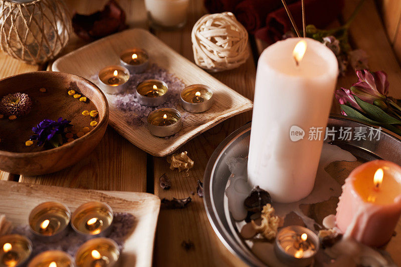 不同大小的燃烧香薰蜡烛和鲜花散布在水疗沙龙的桌子上的特写