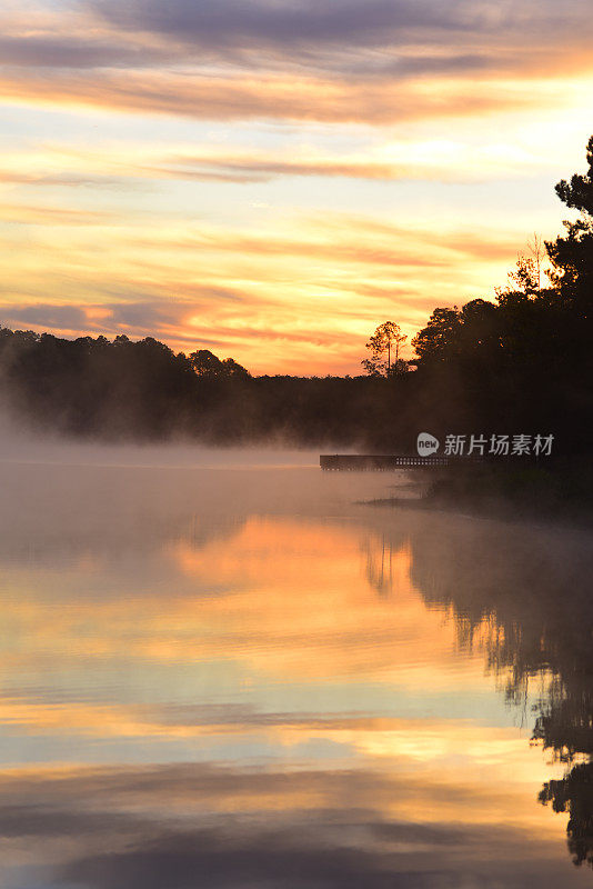 黎明的云和树木倒映在冒着热气的森林湖泊上，还有码头
