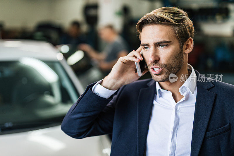 年轻的商人正在汽车修理店打电话。
