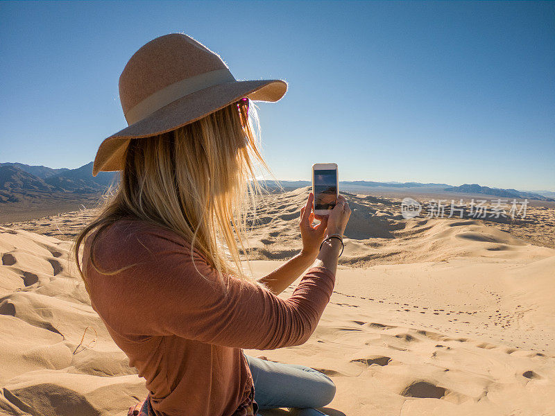 年轻女子旅行时在沙丘上拍摄日落的移动照片