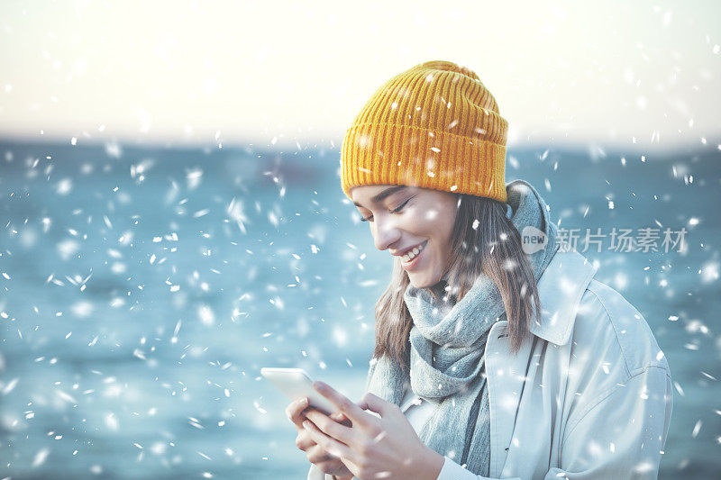 下雪时戴着黄色帽子和手机的年轻女子