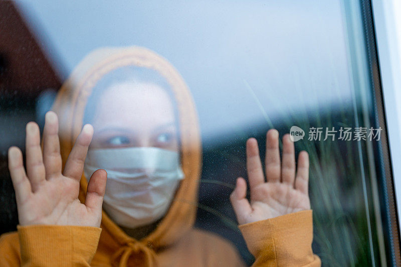 一个戴着外科口罩的少女站在窗前看
