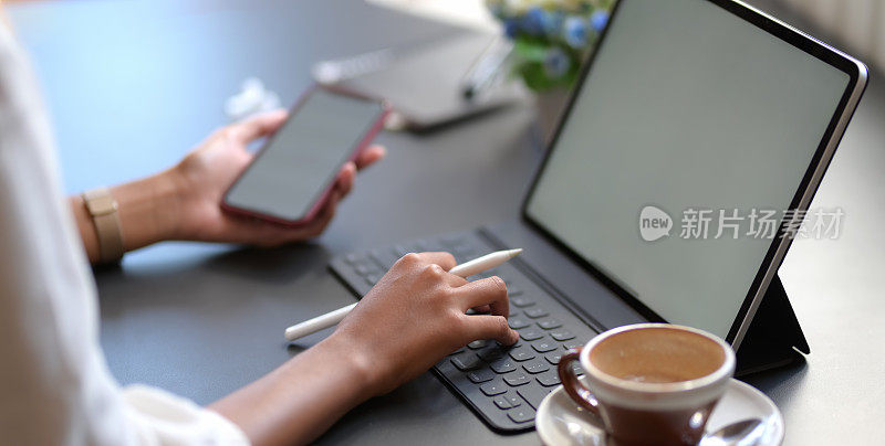近距离观察年轻的女商人在数字平板电脑上打字，同时使用空白屏幕的智能手机