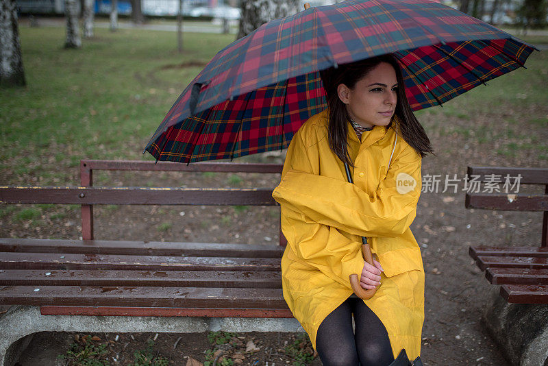 穿着黄色雨衣的年轻女子在公园里度过雨天