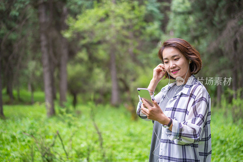 年轻的亚洲女子在森林里戴着耳机听音乐