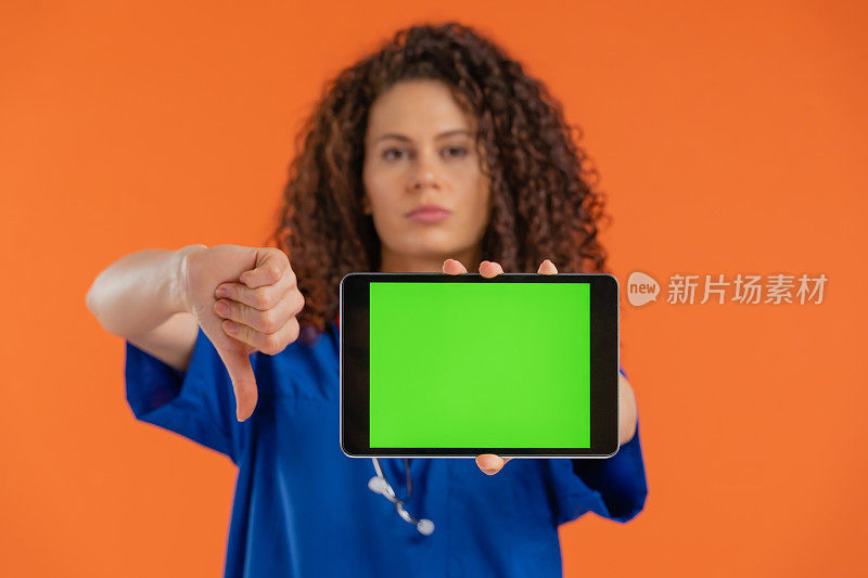 美丽的女医生显示数字平板与色度键绿色屏幕，拇指向下手势，负面情绪