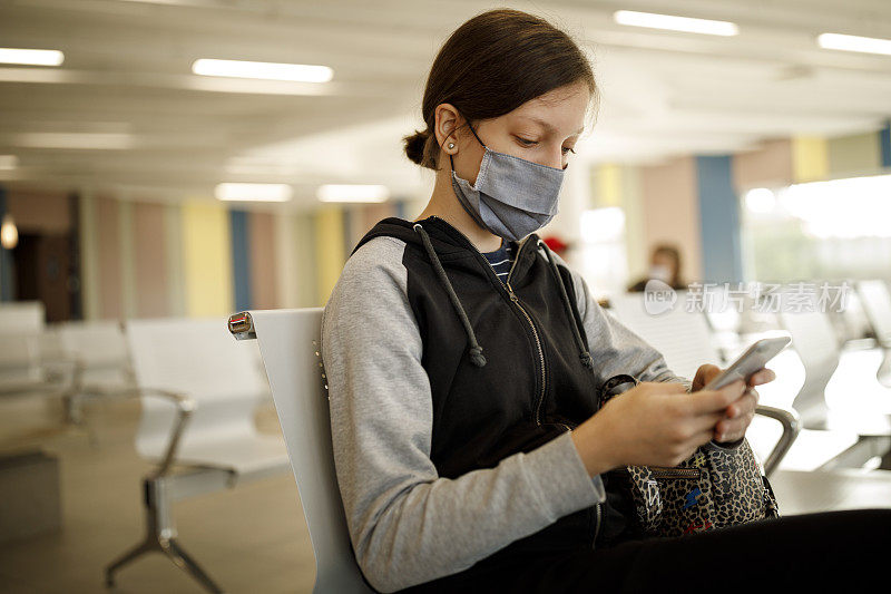 戴着口罩的少女在机场候机时使用手机