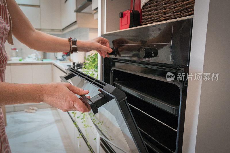 女人打开烤箱做饭。国内厨房的概念。