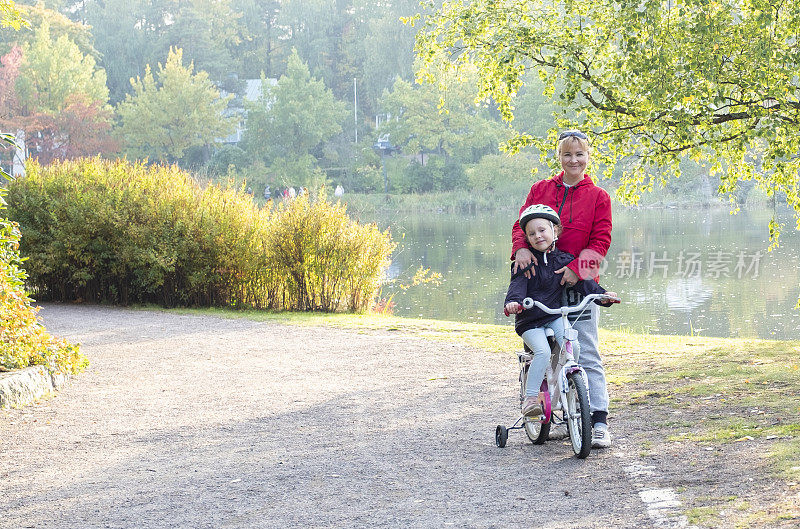 一个白人家庭在秋季公园散步。妈妈拥抱女儿，孩子骑自行车。