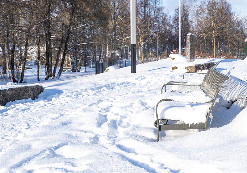 城市公园里的冬天，花园长椅上白雪覆盖。芬兰科特卡市的城市公园。