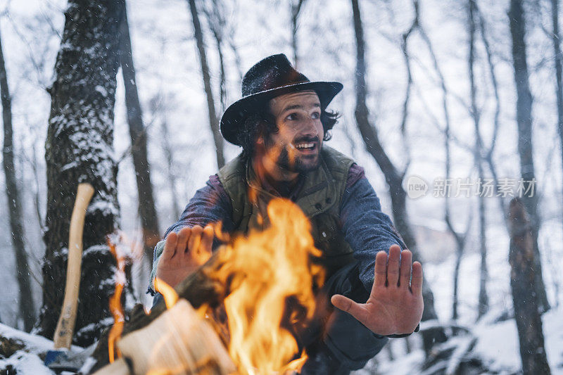 清晨，在白雪皑皑的森林里，年轻人在篝火旁放松