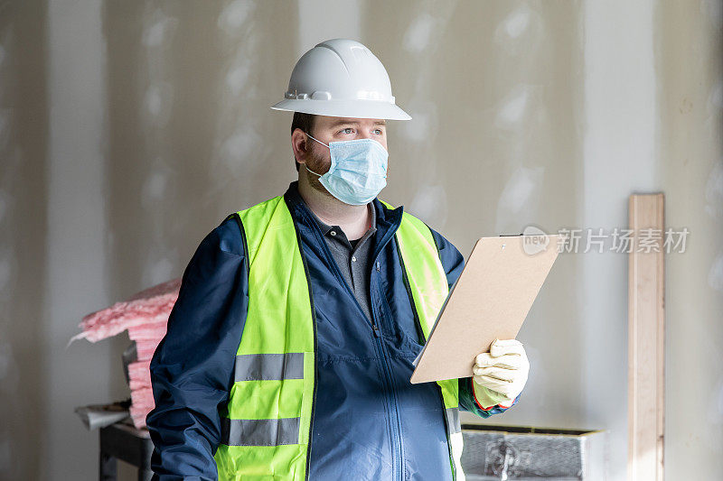 建筑工人或工程师在工地上搬运材料并查看剪贴板上的平面图
