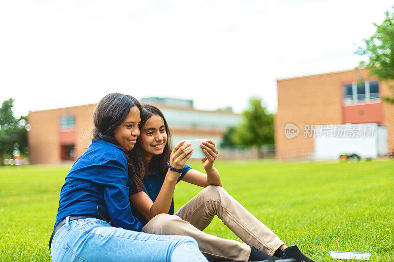 青春期前的女学生坐在校园草坪户外使用技术教育照片系列