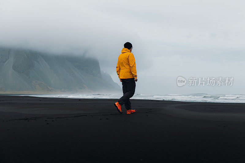 年轻的旅行者探索忧郁的黑色沙滩与山景