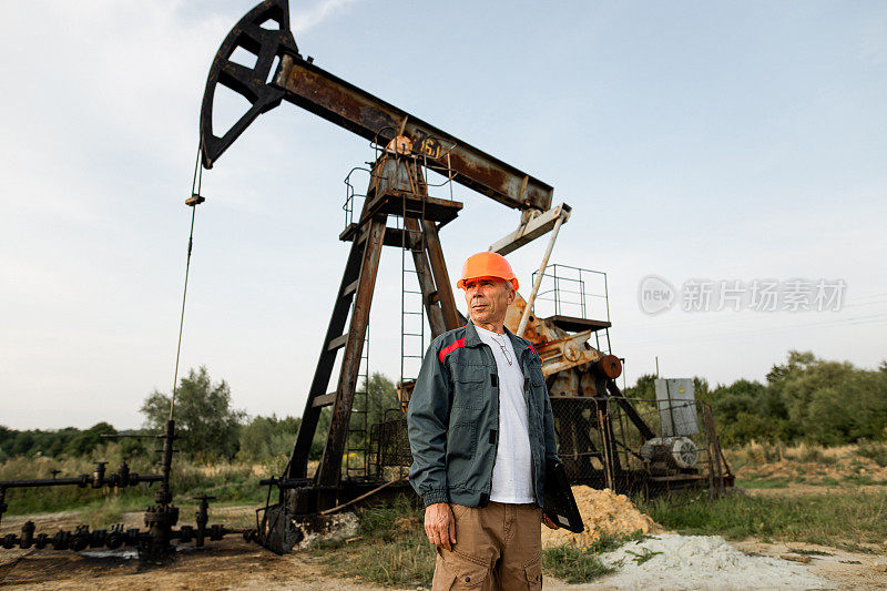 石油工人站在油田油井抽油机前的画像