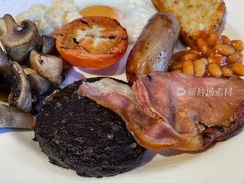 全英式煎早餐培根片，烤香肠，黑布丁，烤番茄，烤豆，蘑菇，土豆泥，煎炒蛋放在白色盘子，聚焦前景