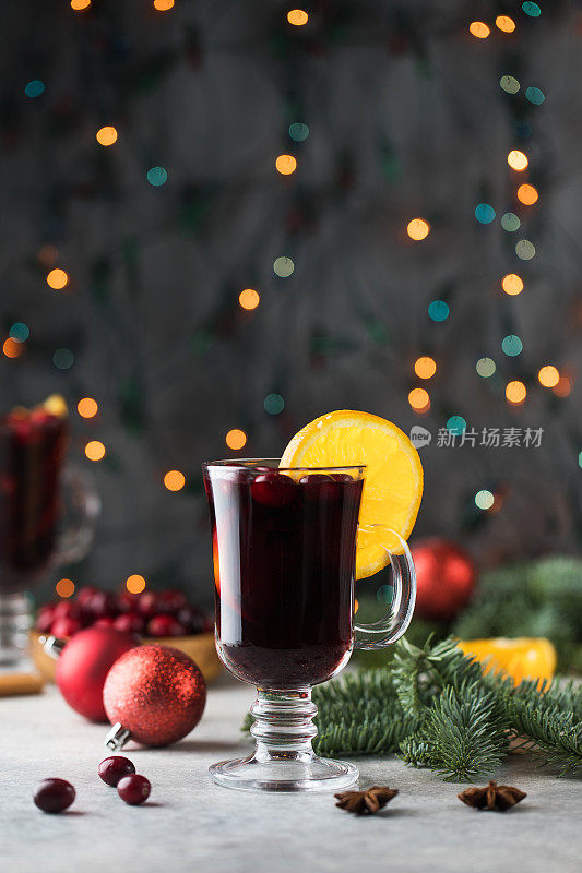 一杯加蔓越莓的热葡萄酒和一根肉桂棒，配以散景的圣诞背景。