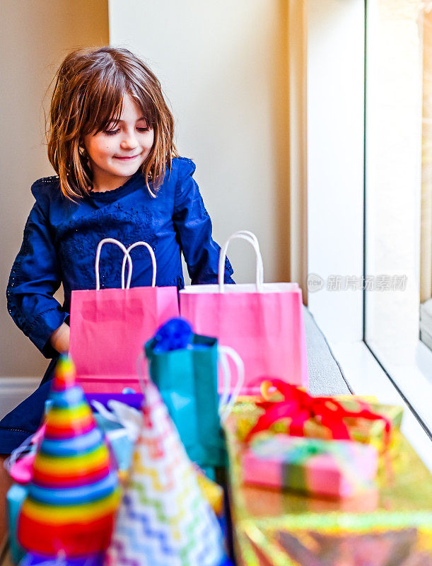 可爱快乐的女孩在她的生日聚会上被五颜六色的礼物包围，傻傻的，微笑着，快乐