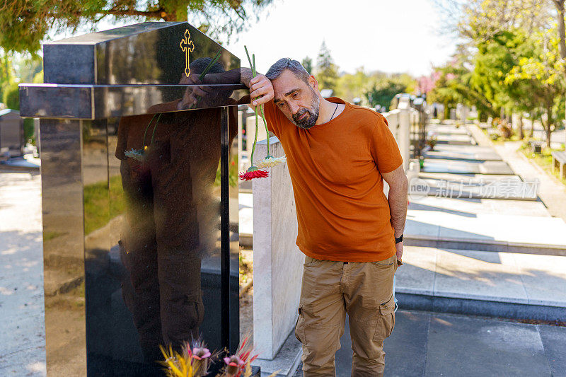 成熟悲伤的男人站在墓地的一块墓碑旁哀悼死者