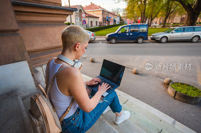 金发短发的年轻女学生拿着笔记本电脑坐在大学外面