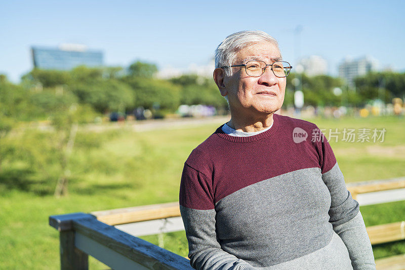 亚裔美国成熟男子享受阳光明媚的一天，靠在栏杆上