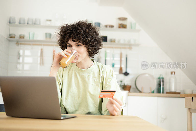 年轻女子在网上购物时喝果汁提神