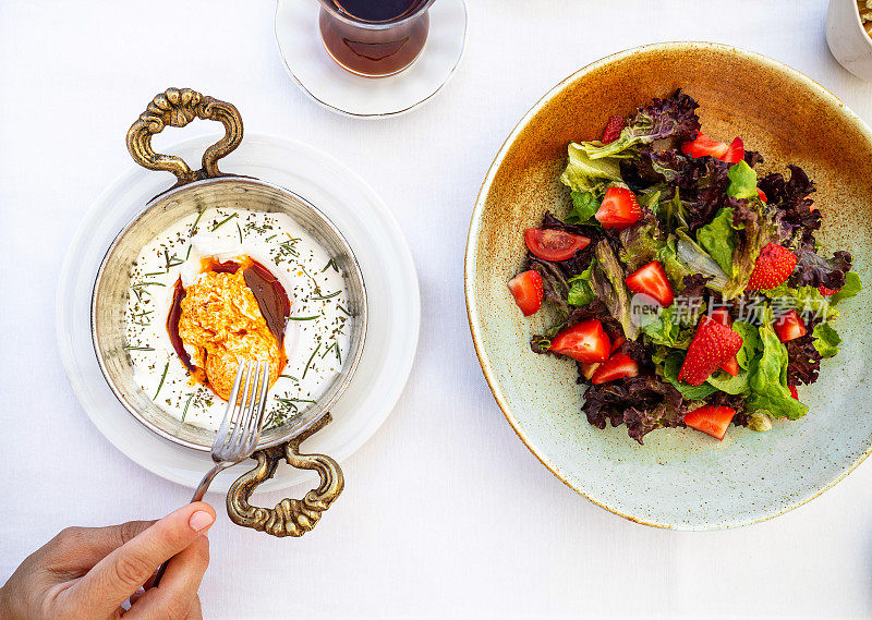 土耳其鸡蛋香菜白碗和新鲜沙拉。土耳其菜系的概念。荷包蛋配酸奶和辣黄油酱。